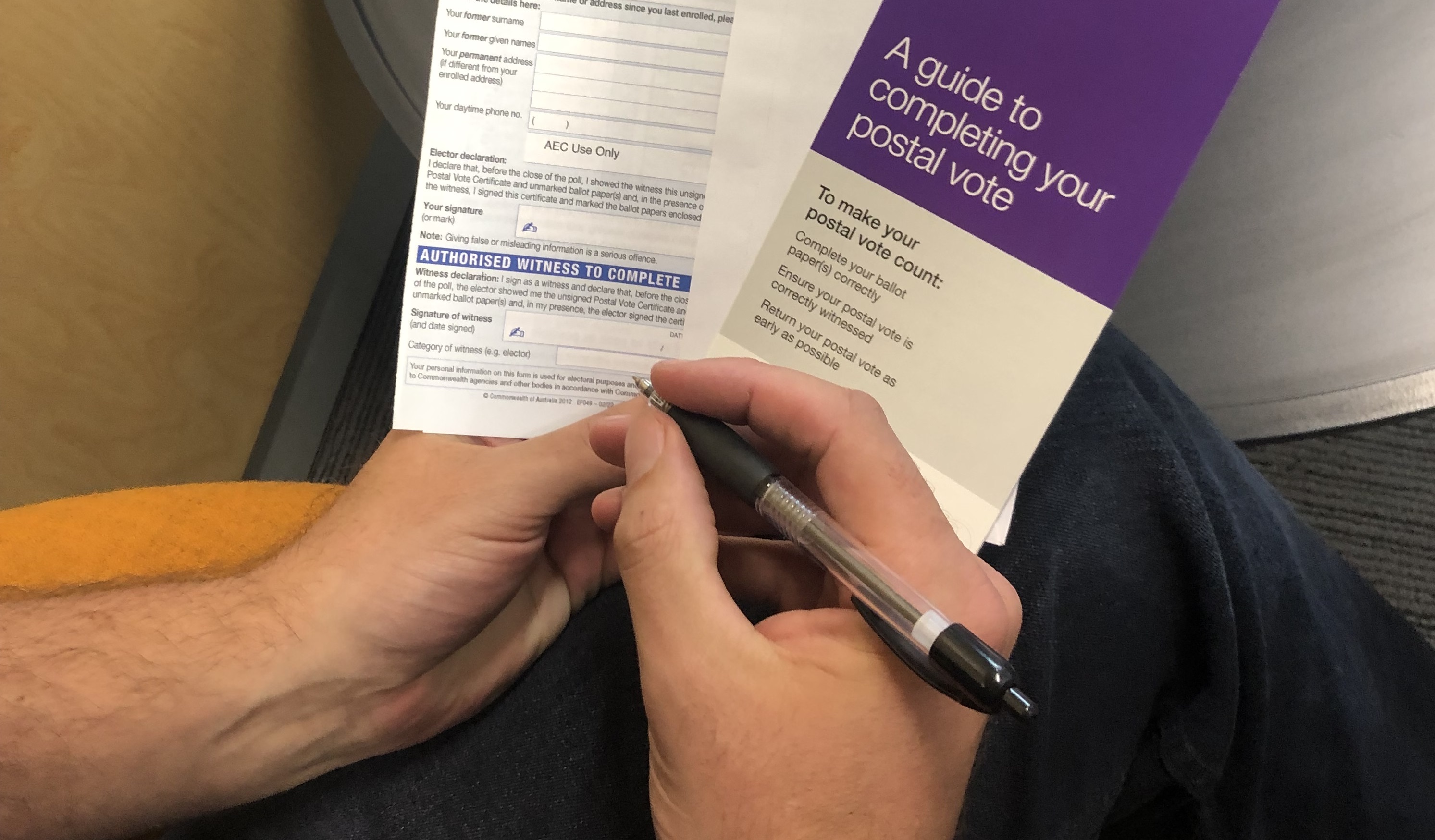 A person holds a pen and a stack of postal vote papers. 